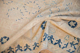 Detail of a vintage Khotan carpet, showing worn ivory pile and small blue geometric patterns.