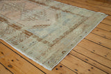 Distressed vintage Oushak rug corner showing muted blue, ivory, and terra cotta geometric patterns.