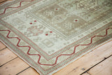 Distressed Oushak rug corner with geometric red border and soft sage patterns.