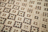 Distressed square and diamond rug motif in ivory, beige, chocolate bronze, and black tones.