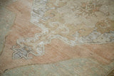 Distressed pile of vintage Oushak rug, featuring faded melon and seafoam colors.