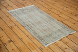 Distressed Turkish Oushak rug edge, featuring ivory fringe and faded charcoal, pale rose pile.