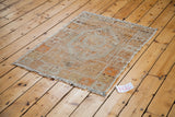 Distressed vintage Oushak rug corner, showing platinum and orange tones with fringed edge.