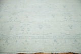 Soft ivory distressed Oushak rug with faded blue-grey border and allover stylized motifs.