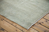 Distressed Oushak carpet corner with even wear, revealing pale sage and silver.