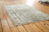 Distressed Oushak rug featuring softened earth tone patterns of ivory, sand, and faded blue.