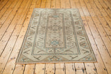 Distressed Oushak rug corner, showing blanched sand, ivory, and subtle blue patterns with short fringe.