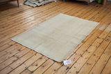 Angled view of a distressed Oushak rug with faded ivory tones and worn fringe.