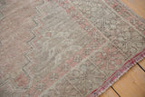 Distressed Oushak rug corner with faded brick rose fringe and tribal zigzag pattern.