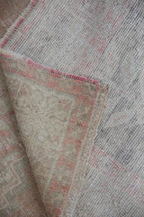 Distressed Oushak rug corner showing faded brick rose pile and woven foundation.