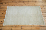Distressed Oushak rug corner with faded ivory and grey texture, showing fringe.