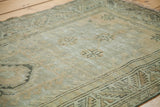 Distressed Oushak rug close-up: muted silver-green field, geometric star patterns, tribal border.