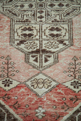 Distressed Oushak rug features geometric and stylized floral motifs in brick, pale rose, and chocolate.