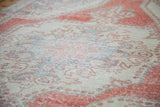 Worn bright Oushak rug's distressed pile, featuring creamy ivory and glowing brick red motifs.