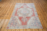 Distressed Oushak rug corner displaying glowing brick red field and creamy ivory motifs.
