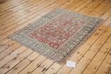 Distressed vintage Turkish Oushak rug corner, showing red field vines and ivory, charcoal border.