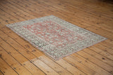 Distressed Oushak rug corner showcasing faded red field with vines and patterned ivory border.