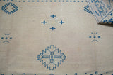 Geometric blue motifs on cream field of distressed Oushak carpet, with folded edge.