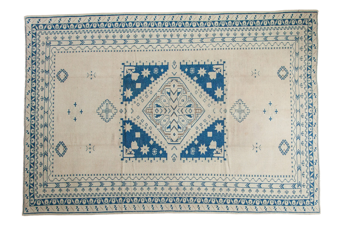 Vintage distressed Oushak rug featuring a geometric blue, tan, and beige medallion with intricate borders, 6'9" x 9'10".