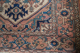 Vintage Serapi rug corner with hand-knotted geometric patterns in softened terra cotta, navy, and teal.