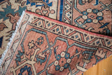 Vintage Serapi rug corner with stylized geometric motifs in terra cotta, ivory, and teal.