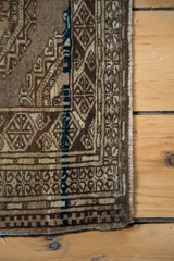 Fringed corner of vintage Turkmen rug, geometric bronze brown gul motif, dark blue accents.