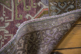 Distressed Oushak rug corner showing hand-knotted foundation and plum, mauve, green pile.
