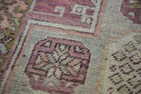 Distressed Oushak runner pile with geometric plum, mauve, ivory, and bronze motif.