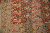 Distressed Birjand rug corner displaying rust red paisley and light-toned floral border.