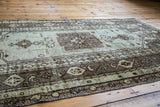 Stylized geometric central medallion and pinwheel border in seafoam and bronze.