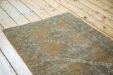 Distressed Afghani rug pile showing faded copper, teal charcoal blue, and ivory patterns.