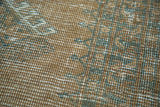 Distressed pile detail of the Afghani rug's faded copper, teal, and ivory patterns.