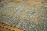 Distressed Afghan rug pile, highlighting faded copper, teal, and ivory patterns.