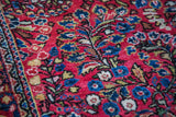 Intricate blossoming blue and white floral motifs on the jewel red pile of a Sarouk rug.