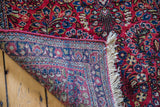 Folded vintage Sarouk rug corner, revealing hand-knotted foundation, fringe, and blossoming floral pile.