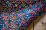 Rolled vintage Persian Bijar rug detail: bright coral rose border with unique blue and green.