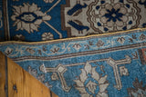Folded antique Caucasian rug showing indigo, teal, and beige arabesque field and border.
