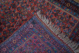 Folded corner of antique Bidjar rug, exposing rich red Herati pattern, floral border, and fringe.