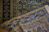 Antique distressed Fereghan rug showcasing intricate blue border patterns and variegated gold tones.
