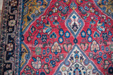 Detailed cranberry red field, blue floral palmettes, and geometric border of vintage Sarouk.