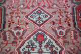 Detail of a vintage Malayer rug's hand-knotted pile showing ivory and red geometric motifs on an abrashed mauve field.