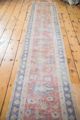Faded red field and blue patterned border of a distressed vintage Oushak runner.