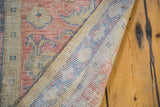 Distressed vintage Oushak runner texture in muted coral, blue, and beige, revealing hand-knotted back.