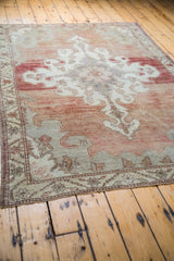 Faded cinnabar red and silvery grey patterns on a distressed Oushak carpet corner.