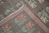 Folded distressed Konya carpet corner shows peach floral motifs, brown field, and pink border.