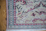 Distressed vintage Oushak runner corner with pastel ivory field and green geometric border.
