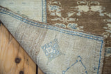 Folded corner of vintage Oushak rug, showcasing its tightly hand-knotted foundation in silvery beige and blue.