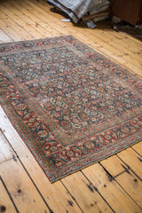 Antique Tabriz rug corner displaying a classic rusty red border and indigo blue Herati motif.