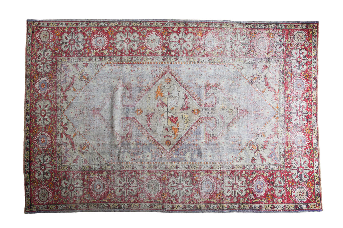 Distressed vintage Oushak carpet with faded ivory and grey medallion, framed by brick red floral borders.