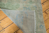 Distressed Oushak rug showing its faded green pile, blue plant motif, and woven foundation.